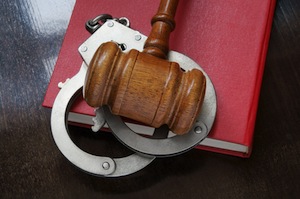 Gavel and handcuffs with red legal book on wooden table