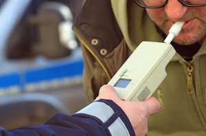 Alcohol testing, man blowing in breathalyzer